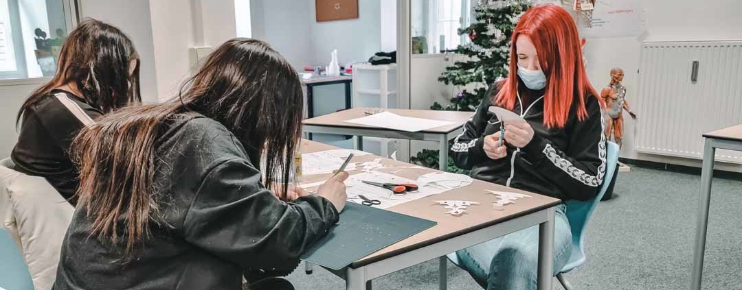 Schüler sitzen am Tisch und fertigen Scherenschnitte